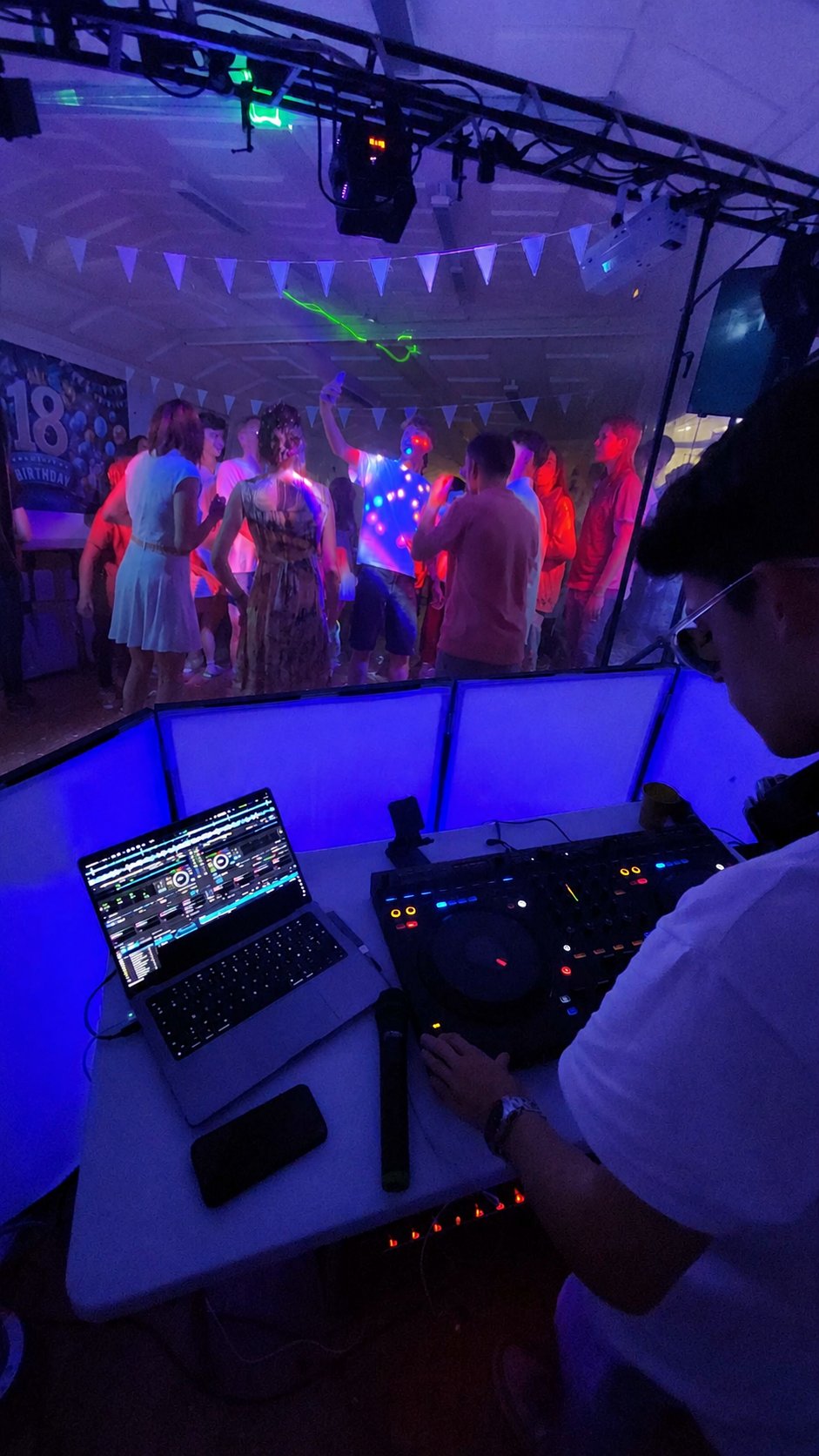Dj Nøva en régie pendant une soirée d'anniversaire, ambiance lumière bleue et danseurs en fond